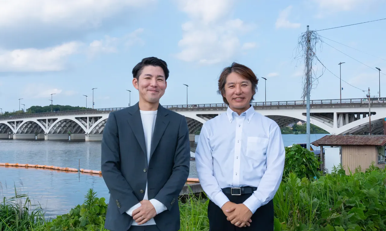 手賀沼を背景に立っている柏市沼南商工会の諸橋さんと染谷